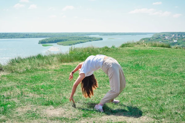 Slim beautiful woman doing yoga and stretching outdoors. young woman exercising alone on a river bank. person enjoying summer active lifestyle — Stock Photo, Image