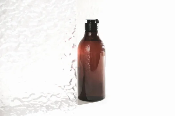 Shower gel in an amber plastic bottle next to bathroom transparent door. bottle with water drops in sunlight. copy space. hygiene and daily self care routine concept — Stock Photo, Image