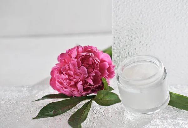 Crema facial cosmética blanca en una botella de vidrio. peonía flor y ducha puerta. baño blanco. cuidado personal y tratamiento de belleza — Foto de Stock