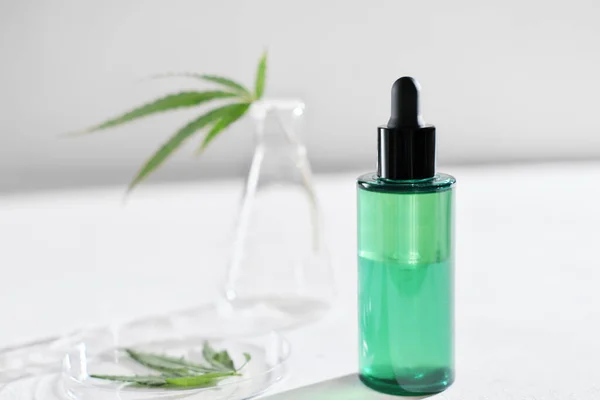 cannabis face serum in green bottle and hemp leaves in laboratory . petri dish and glassware on lab table. dermatology concept, alternative treatment. front view.