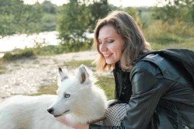 Nehir kıyısında köpeğini kucaklayan mutlu bir kadın. Yakutian Laika yana bakıyor. Hayvan arkadaşları, açık hava aktiviteleri ve hayvan bakımı.