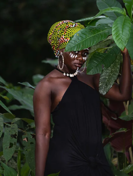 African woman standing in the real jungle with tribe marks on her face and African colors as headdress, Photo taken in Ghana West Africa