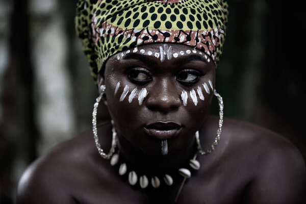 African woman sitting in the Aburi forest in Ghana with white painting on her face and headdress
