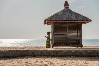 Afrika kıyılarında Afrika giysileri içinde Keta Gana Batı Afrika 'da bir bungalovun yanında tek başına duran Afrikalı kadın.