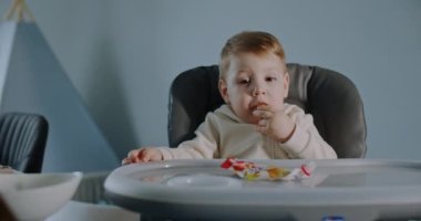 Hungry little boy sitting in a stroller, fed by his mother at home. Slow motion.