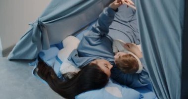 The young mother and the child are playing, lying in a tent in the house,