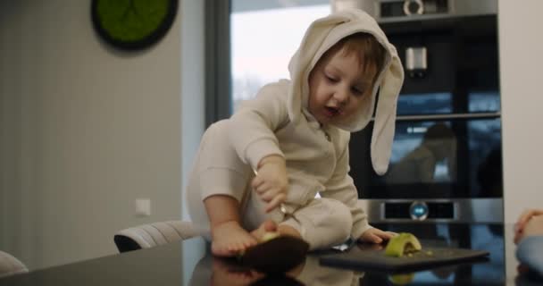 Criança pequena, bonita e feliz come abacate na cozinha ao lado de sua mãe. — Vídeo de Stock