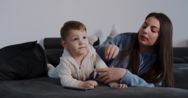 Junge, müde Mutter mit kleinem Kind liegt und ruht vor dem Fernseher — Stockvideo