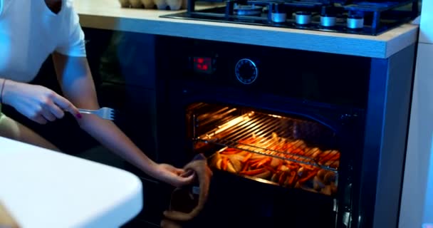 Uma menina cozinha comida no forno na cozinha em casa à noite. Movimento lento. — Vídeo de Stock