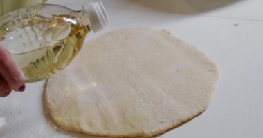 Bir kadın mutfakta çiğ hamura ayçiçeği yağı döküyor..