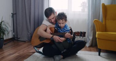 Babam küçük çocuğa evdeki oturma odasında gitar çalmayı öğretiyor..