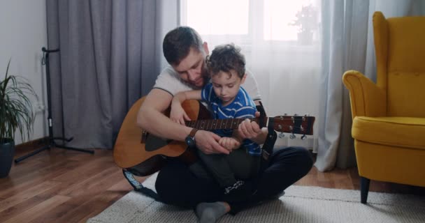 Babam küçük çocuğa evdeki oturma odasında gitar çalmayı öğretiyor.. — Stok video