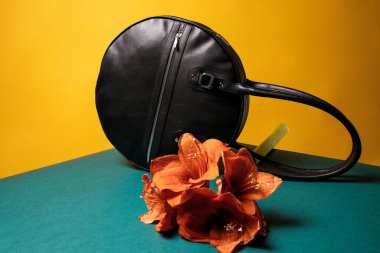 A black leather bag, on a yellow background in a minimalist style, flower decor.