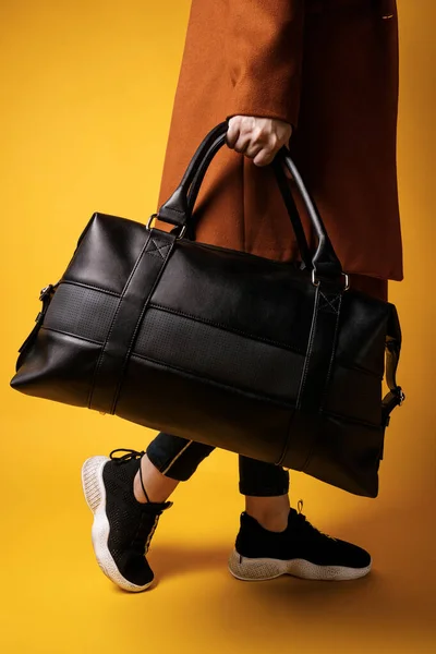 A black leather bag in the hand of a girl model, on a colored background.