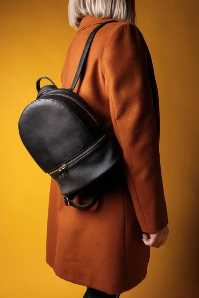 A black leather bag in the hand of a girl model, on a colored background.