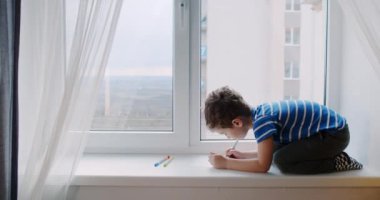 Küçük bir çocuk, mutlu bir çocuk, evdeki pencere pervazına resim çiziyor..