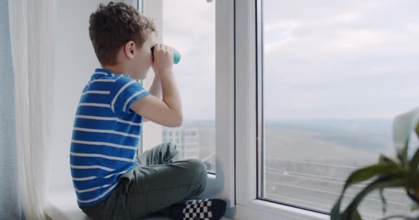 Um menino pequeno olha com binóculos na janela em casa. Domingo dia. — Vídeo de Stock