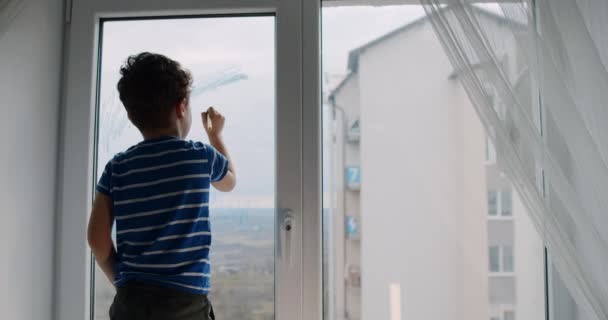 A little boy draws on the window glass alone at home in the apartment. — Αρχείο Βίντεο