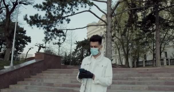 A young man, wearing a face mask in the city, sunset, talking on the phone. — Stock Video