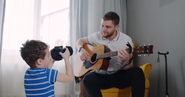 Dad is pictured by his little blogger son playing the guitar. — Wideo stockowe