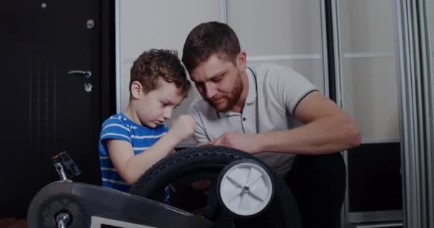 Le jeune père aide son fils à réparer le vélo avec des outils dans la maison. — Video