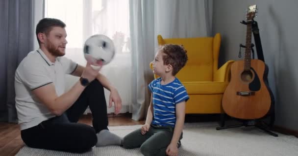 Junger Vater und sein Sohn mit lockigem Haar spielen Fußball. — Stockvideo