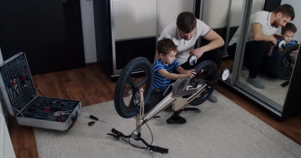 어린 아버지는 아들 이 집안에서 도구로 자전거를 수선하는 것을 도와 줍니다. — 비디오