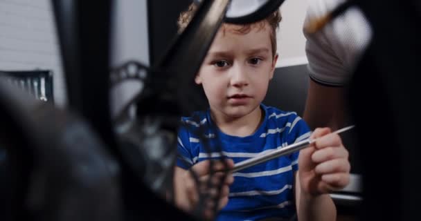 Весёлый мальчик в доме, чинит сломанный велосипед инструментами — стоковое видео