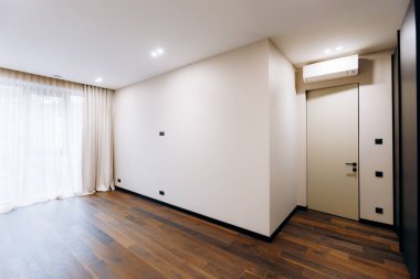 This spacious minimalist room showcases beautiful wooden flooring and is filled with ample natural light throughout