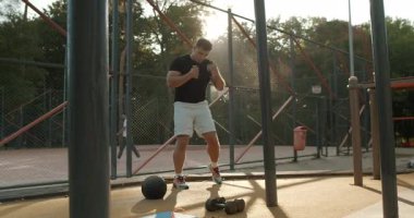 An athlete is engaged in an intense workout session at sunset, performing exercises in a fitness park environment