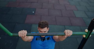 A highly determined young man showcases his impressive strength by performing pullups in a public outdoor fitness area