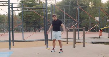 A man is actively performing dynamic fitness exercises using resistance bands in an outdoor fitness park setting