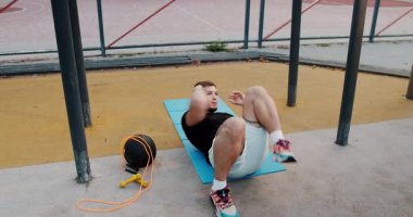 A young man demonstrates crunch exercises on a mat in a park, focusing on fitness and healthy routines