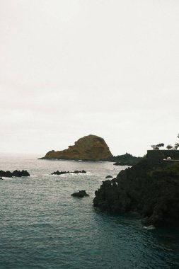 Sakin sahil manzarası, kayalık oluşumlu huzurlu kıyı şeridi, sessiz tonlu sakin deniz manzarası ve yumuşak dalgalar.