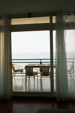 Deniz kenarındaki sabah sükuneti, huzurlu okyanus manzarası üzerinde gün doğumu yumuşak güneş ışığı ve oturma düzeniyle sessiz teras.