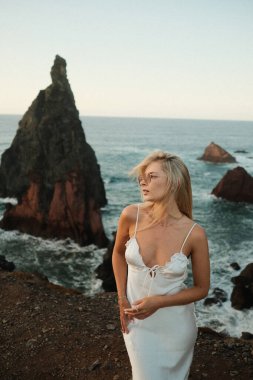 Deniz kenarındaki uçurumda gelin, okyanus manzarasına bakan zarif gelin, gün batımında aydınlanan gelin dramatik kayalıklara bakıyor.