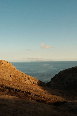Huzurlu kıyı manzarası, sakin mavi suların üzerinde gün batımını rahatlatan bir tepe manzarası minimum bulutlar ve sürüklenen bulutlar.