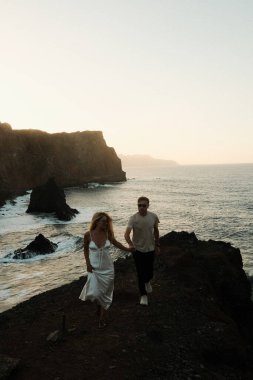 Kıyı yürüyüşünde gülümseyen çiftler, keyifli ortaklar, sıcak akşam güneşinin tadını çıkararak kıyı şeridi boyunca yürüyüş yaparlar.
