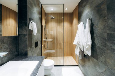 Spa inspired ensuite with warm wood accents, large glass shower, floating vanity, soft lighting, plush robes on wall hooks, stone