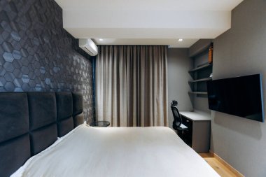 Çalışma masalı sessiz bir süit yatak odası, yastıklı yatak başlığı, duvara monte edilmiş televizyon, sandalyeli masa, karartma perdeleri.,