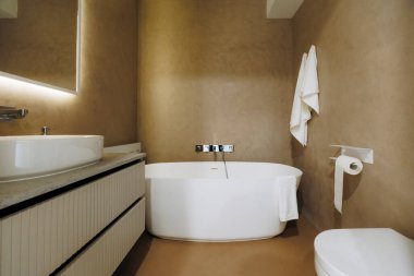 Serbest küvetli kaplıca banyosu, aşırı büyük havuz kibri, yumuşak ortam aydınlatması, sıcak nötr alçı duvarlar, peluş.