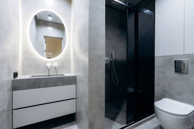 Yuvarlak aynalı modern banyo, beton kibir ve cam duş yumuşak atmosferli huzurlu bir spa atmosferi yaratıyor.