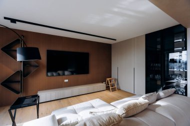 Duvara monte edilmiş televizyonlu şık bir medya salonu. Koyu renk aksanlı duvar ve heykel raf çerçeve ekranı, yer lambası görevi sağlıyor