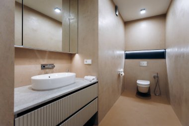 Tezgahı lavabolu sıcak modern banyo. Yumuşak lamba parıltısı ve aynalı dolap duvar kaplamasını, krom musluğu yansıtır.,