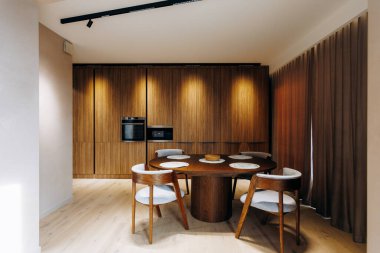 Sıradan yemek için yuvarlak ahşap yemek masası. Kıvrımlı sandalyeler orta süsü, sıcak kabin arkaplanı, doğal ışık