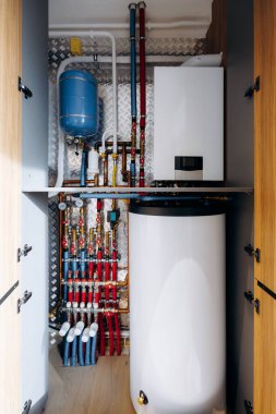 Kazan tankı ve manifoldlu kompakt malzeme dolabı, bakır borular ve mavi genişleme kabı görünür, beyaz silindir su ısıtıcısı