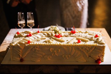 Masada süslü beyaz pasta süsü, borulu tereyağı kırmızı kirazlı garnitür eşleştirilmiş şampanya bardaklarının yanında, ılık
