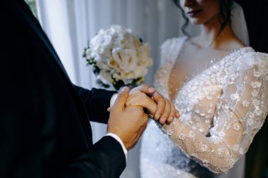 Samimi düğün anı, çiçeklerin yanında el ele tutuşan çift, otantik düğün sahnesi, dokunaklı el teması.