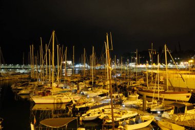 Parlak şehir manzarasının altındaki sessiz marina suya, sakin yüzeye yansıyan ışıklarla sakin liman sahnesine yansıyor.