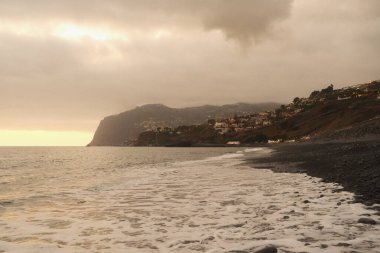 Fırtınalı sahil sahnesi, dalgalar kayalık kıyılara çarpar, uçurumlar derin derin derin gri gökyüzünün altındaki çalkantılı sulara bakar.